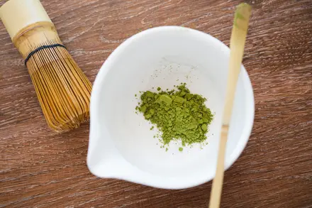 A ceremonial matcha bowl with a bamboo whisk and scoop of stone-ground matcha.